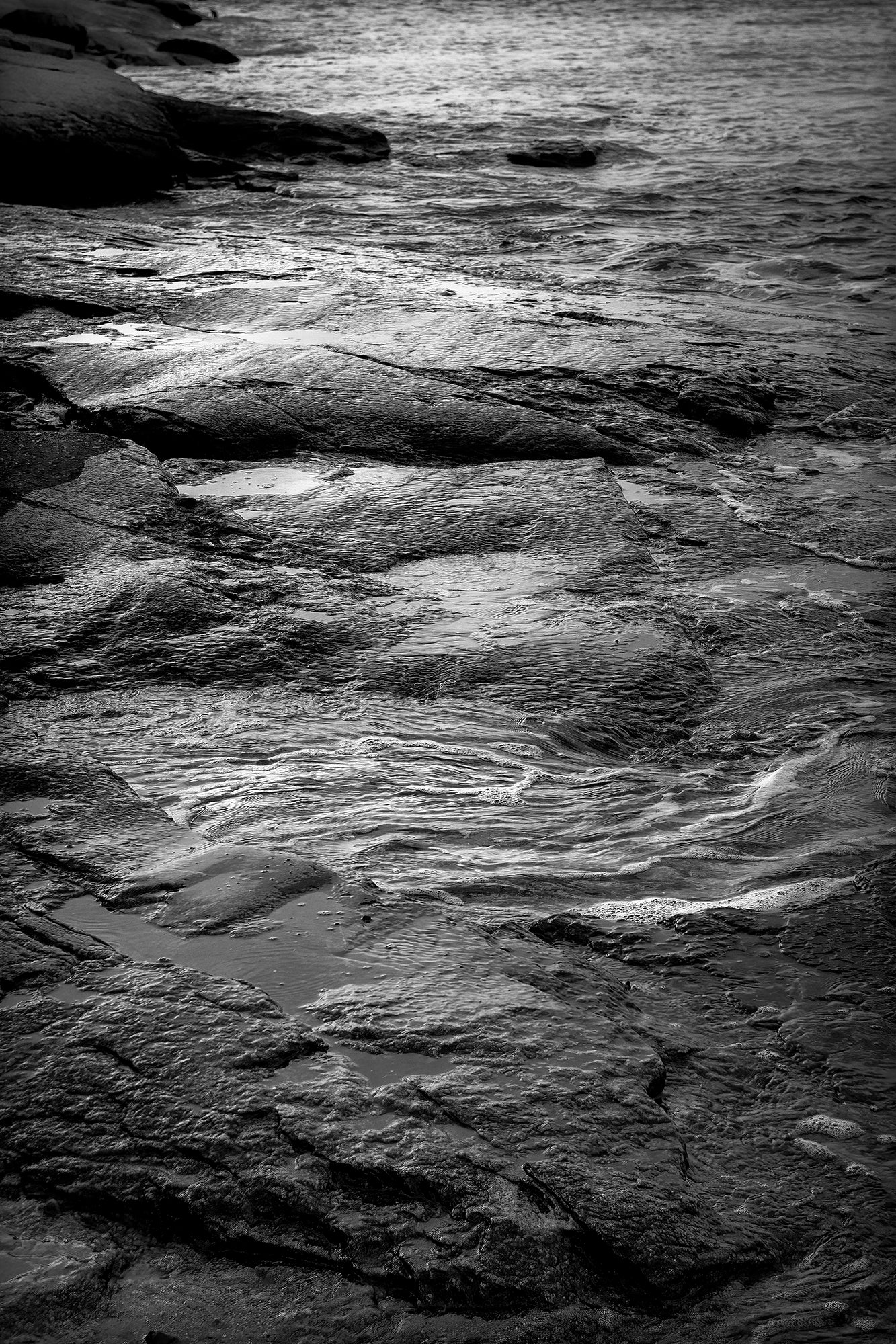 Black and white coastal detail of tidal water flowing over granite rocks at Cushing Maine with textured shoreline and soft tonal contrast