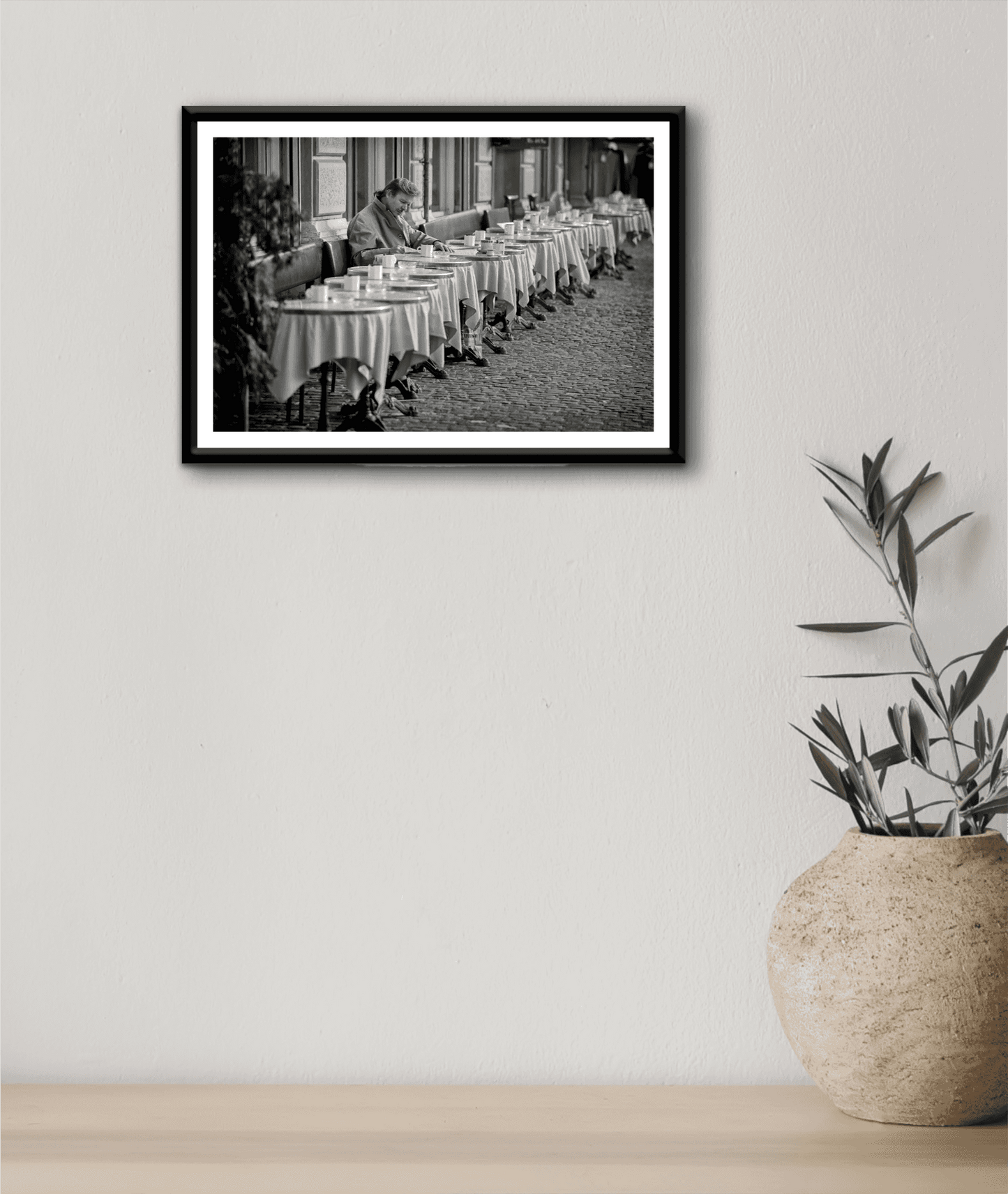 Zurich Series #3 – The Man at the Café, Zurich in Black and White – Fine Art Print by Michael Hart hung on a neutral wall with a ceramic vase. A serene monochrome artwork enhancing minimalist interior aesthetics.