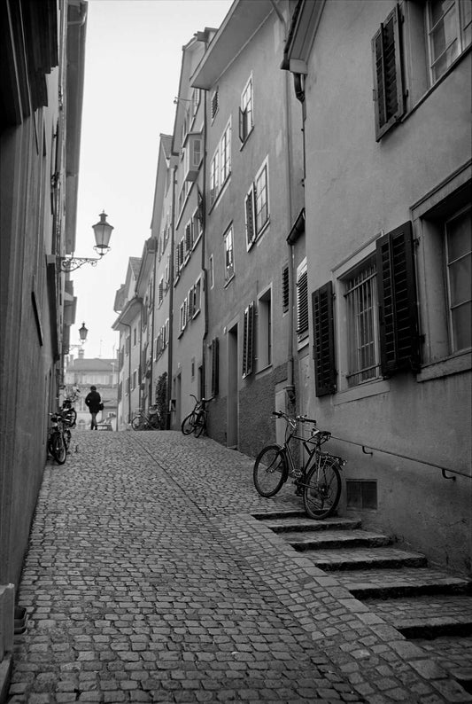 Solitary figure walking up a cobblestone street in Zurich, Switzerland, captured in black and white with strong perspective and architectural depth
