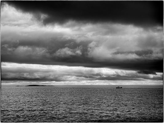 Black and white seascape of the Atlantic Ocean off Marshall Point, Maine, with dramatic storm clouds and a small boat on the horizon