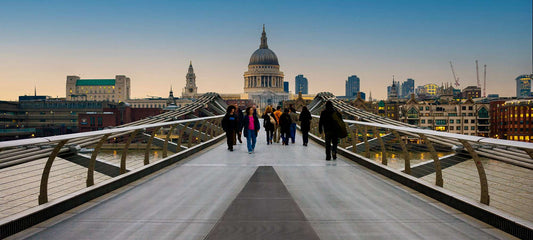 Fine art photograph of Millennium Bridge in London at twilight, with pedestrians crossing toward St. Paul’s Cathedral and city lights emerging.