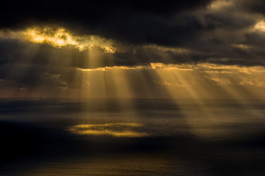 Sunrise from Cadillac Mountain in Acadia National Park with dramatic sun rays breaking through clouds and illuminating the Atlantic Ocean below.