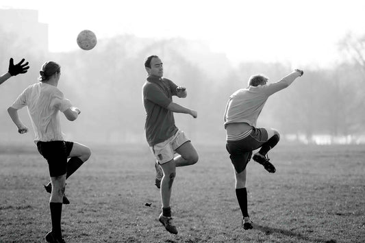 Still Kickin — black and white street photograph of amateur soccer players mid-action in Hyde Park, London, captured in soft atmospheric light