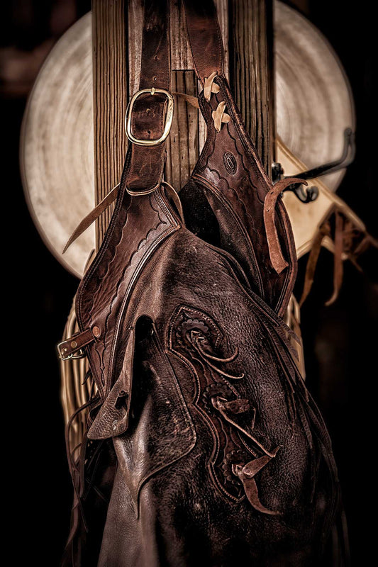 Sepia-toned still life of ranch tack—leather saddle, bridle, and hat hanging inside a Texas barn at 44 Farms.