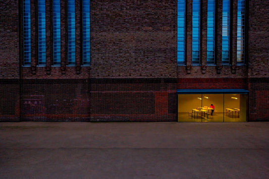 Twilight view of the Tate Modern in London with blue window reflections and a lone figure in warm light inside the gallery.