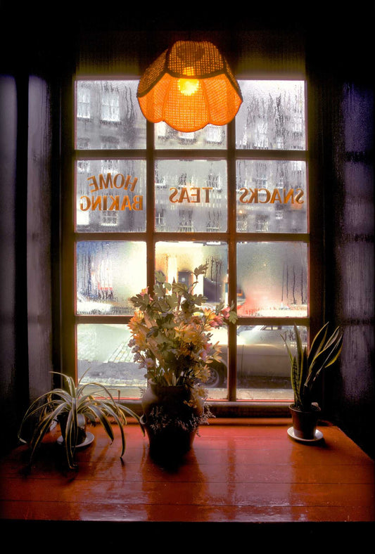 Fine art photograph of a café window on Edinburgh’s Royal Mile with misted glass, warm interior light, and flowers on a windowsill, captured on Kodachrome.