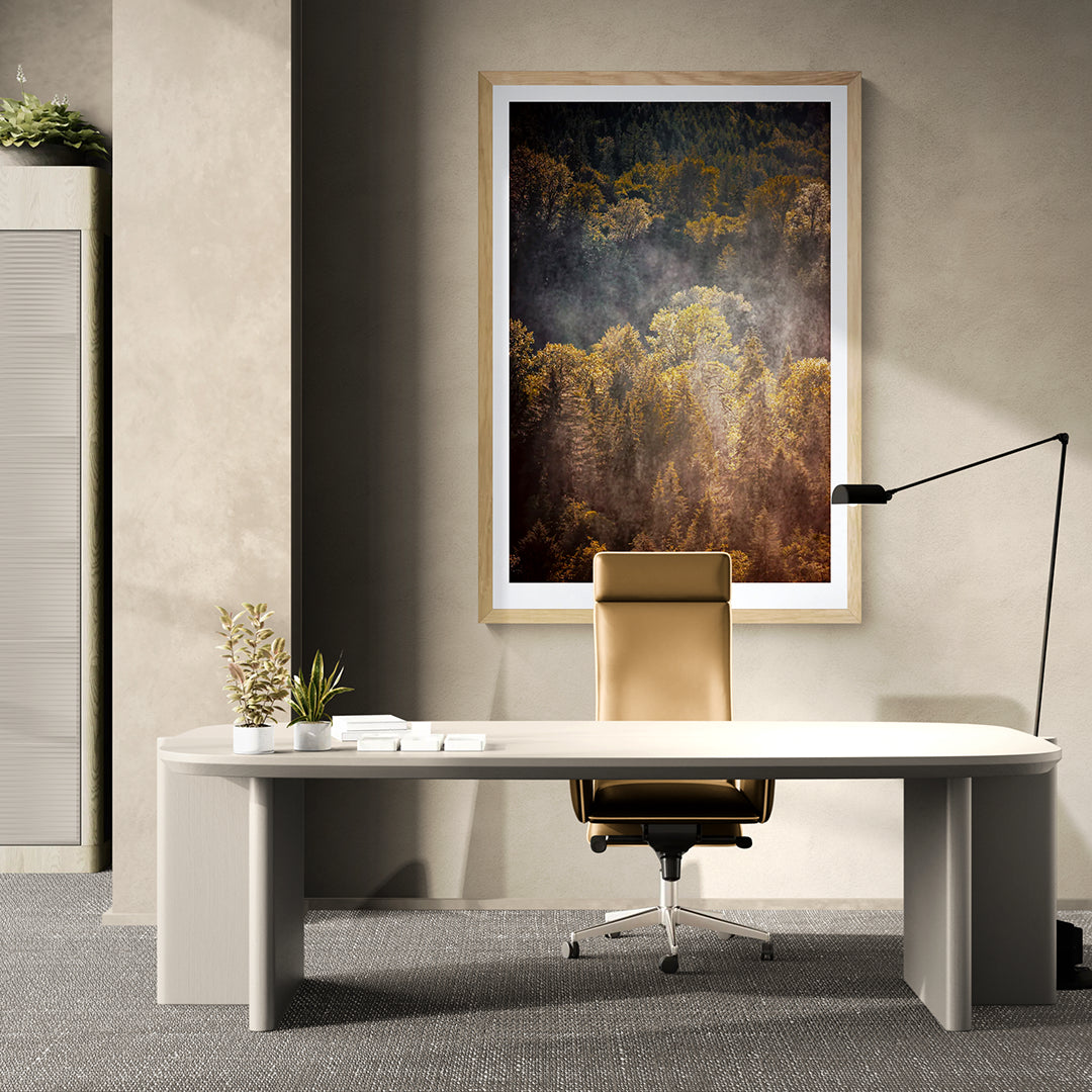 The Forest Illuminated fine art photograph displayed in a light wood frame above a modern office desk in a minimalist, neutral-toned interior.