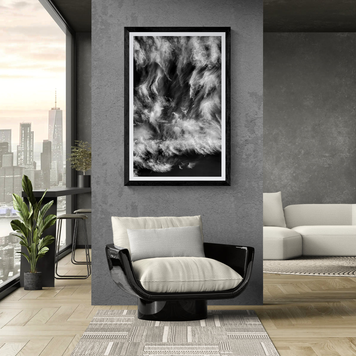 Black and white fine art photograph of swirling cirrus clouds and a small crescent moon displayed on a gray feature wall beside a modern lounge chair in a contemporary living room with floor-to-ceiling city views.