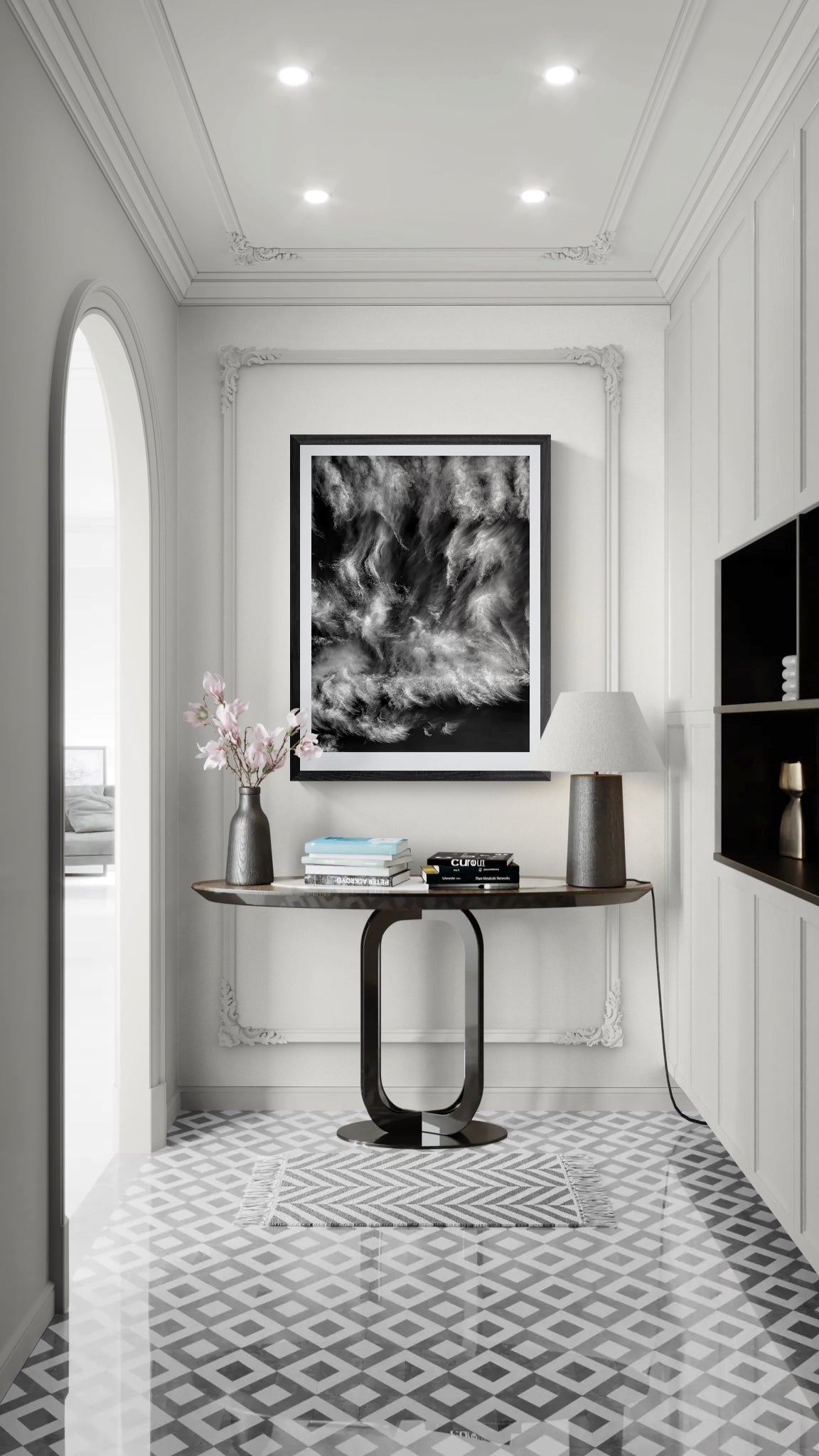 Black and white fine art photograph of swirling cirrus clouds and a small crescent moon displayed in a black frame above a console table in an elegant, light-filled entryway.