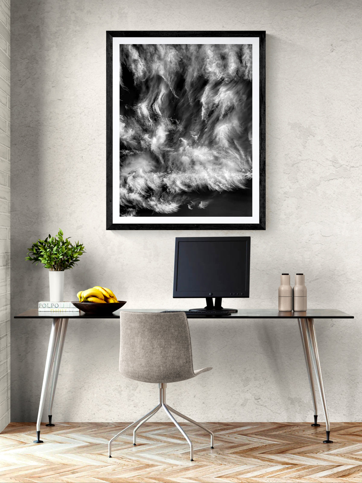 The Moon Watches the Ride, a limited edition black and white photograph of swirling clouds and a crescent moon, displayed in a black frame above a desk in a contemporary home office.