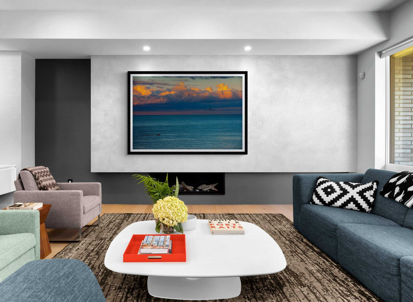Modern living room featuring The Race – Small Boat and Birds in a New England Coastal Sunset framed print as a centerpiece above a sleek fireplace.