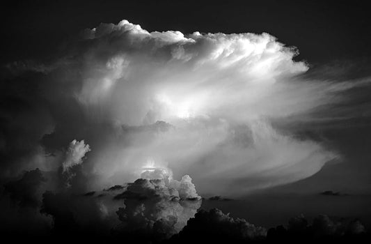 Black and white photograph of a towering thunderhead cloud illuminated from within over Magnolia, Texas, showing dramatic light rays and layered storm structure