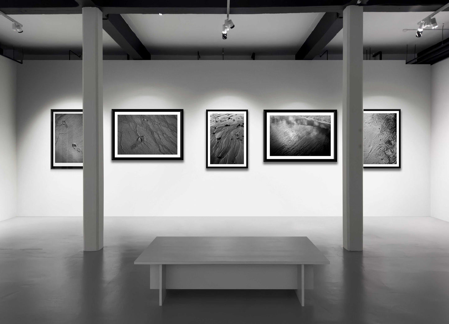 Gallery wall featuring 'Traces #3' and other black and white sand prints, showcasing fine art coastal photography in a modern exhibition space.