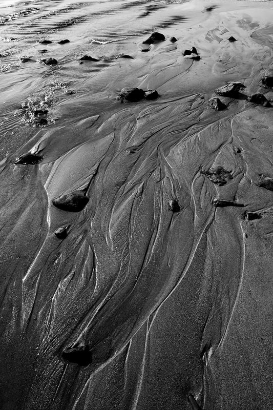 Black and white photograph of tidal sand patterns on the Maine coast, showing flowing water-formed lines and abstract coastal textures.