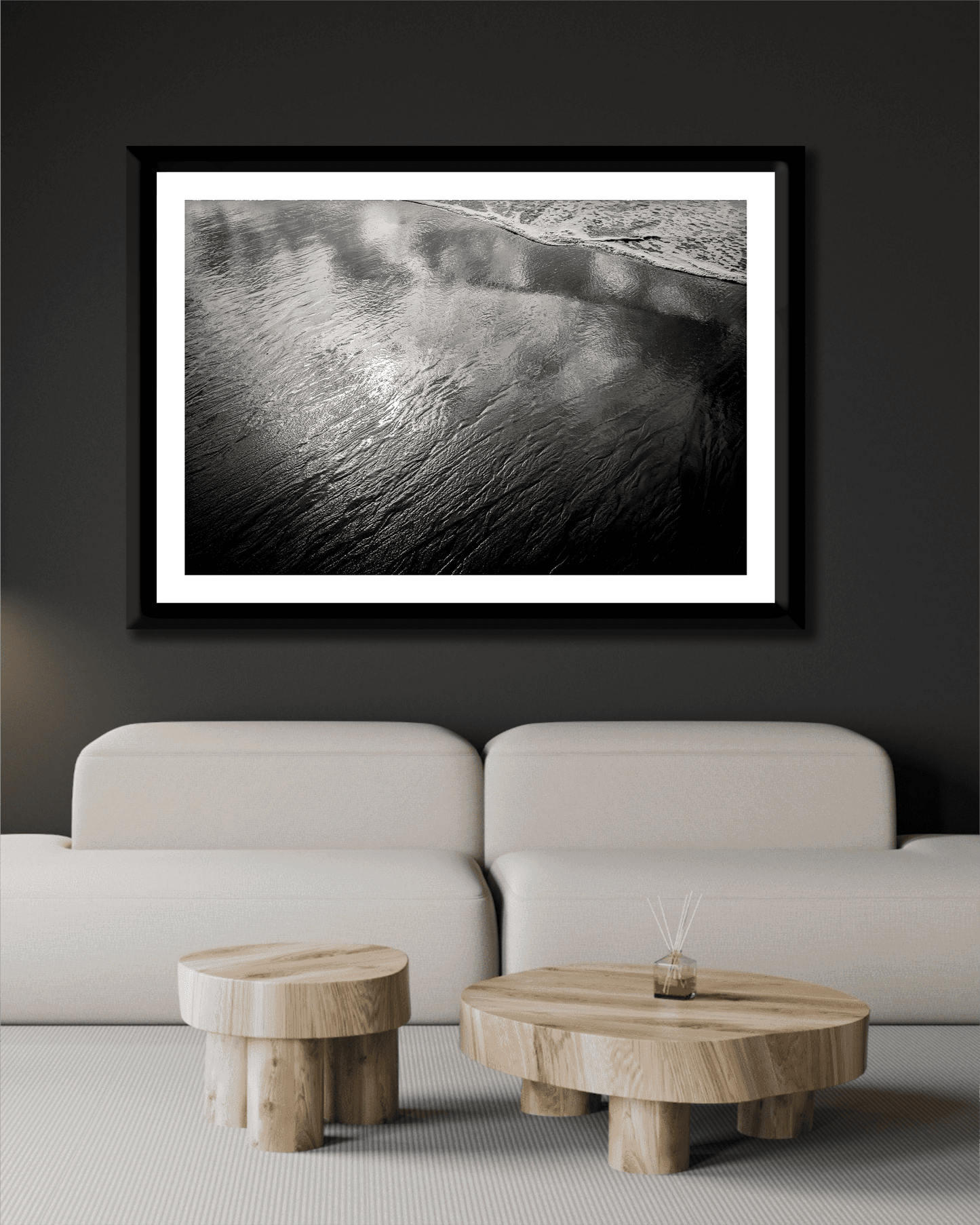 Contemporary black wall decor with framed 'Traces #4 – Reflections at the Sea Edge, Maine' above cream sofa and wooden coffee tables in minimalist style.