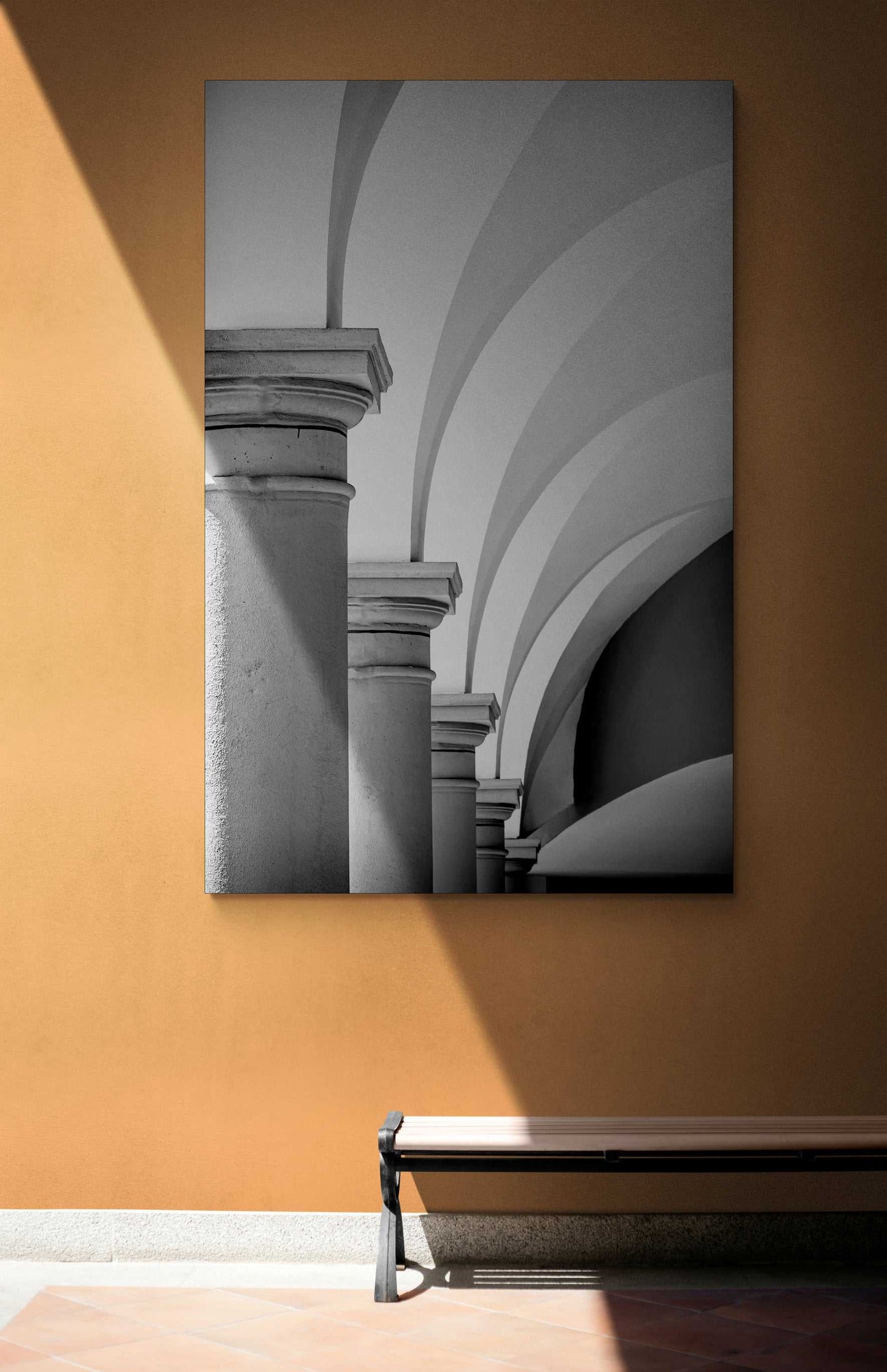 Arches, Barberino – Limited Edition Black and White Photograph of Italian Architecture displayed on a terracotta wall with a bench below. Vertical composition highlights Tuscan arches and classical columns in soft monochrome tones.