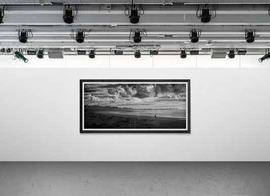 Framed black and white panoramic photograph of a person and dog on Monterey Bay displayed on a modern gallery wall