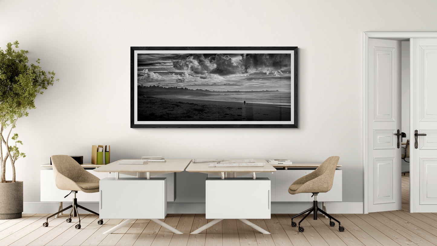 Black and white panoramic coastal photograph displayed as wall art in a modern office workspace