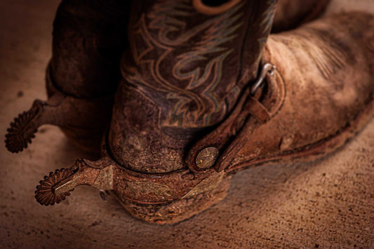 Close-up of well-worn cowboy boots with spurs on a Texas ranch floor, showing aged leather, dust, and working patina.