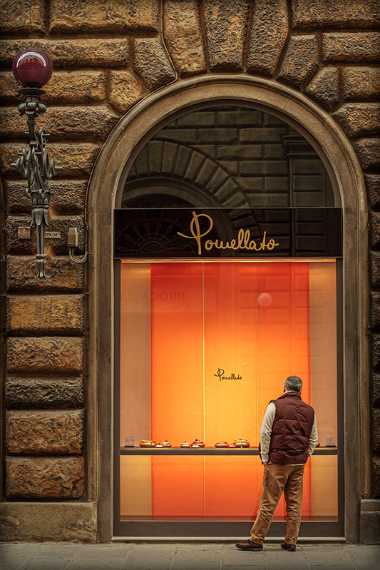 Man pausing at a glowing jewelry window in Florence, Italy, framed by stone architecture and warm evening light.