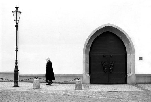Woman walking past a church door and lamppost in Zurich, Switzerland in a minimalist black and white street photograph