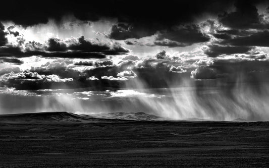 Black and white landscape photograph of rainstorm and virga sweeping across Wyoming plains beneath dramatic cloud formations.